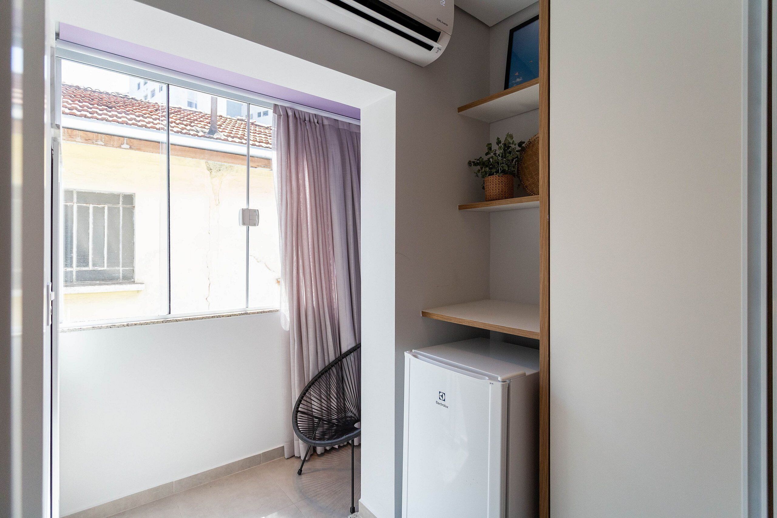A compact room with a sliding glass door leading to a balcony, a small refrigerator, and a chair.