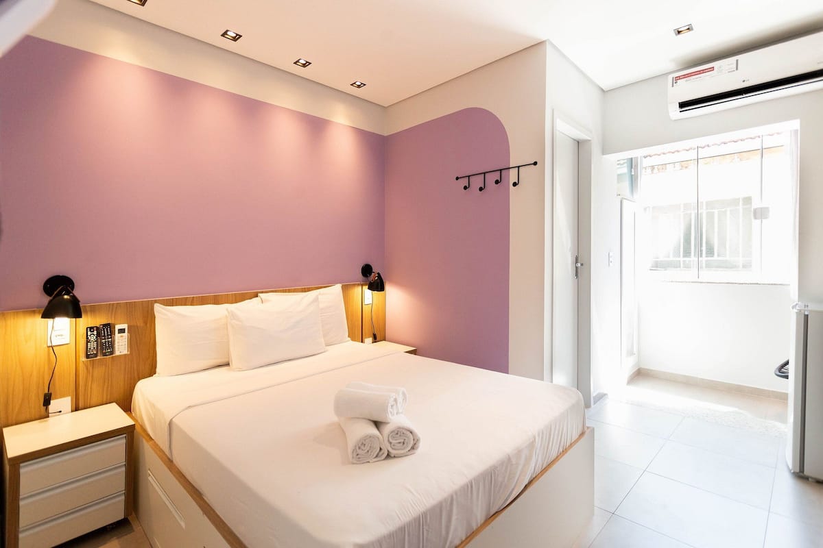 Une chambre d’hôtel avec un lit, des lampes de chevet, une table de nuit, un téléphone fixé au mur et une fenêtre avec des rideaux.