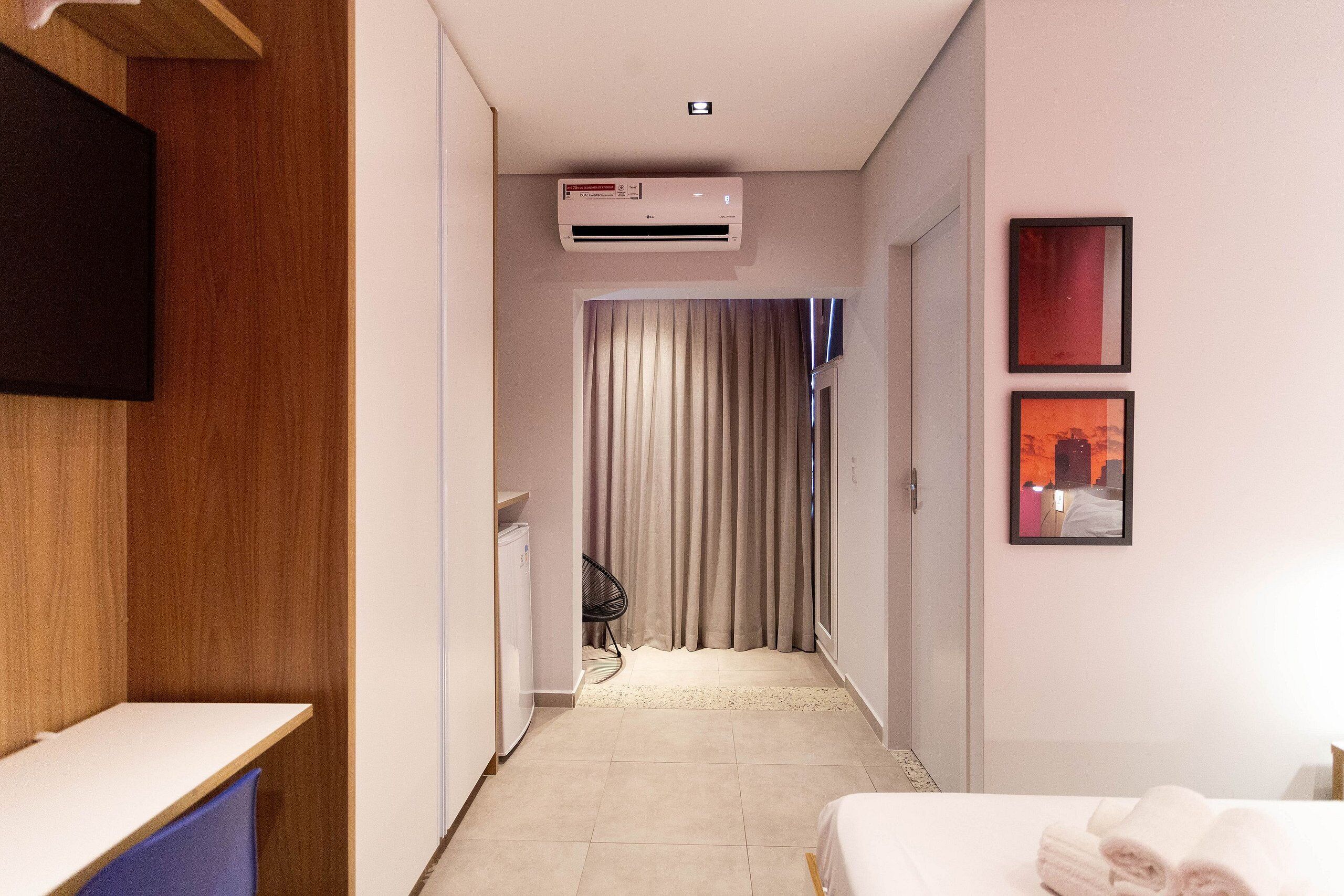 A hotel room with a bed, a desk, an air conditioning unit, a TV, and a door leading to another room.