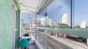 Un balcón con vistas a una calle de la ciudad, una mesa con sillas y una barandilla de cristal.