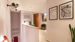 Un pasillo con un mostrador de recepción, una silla verde y dos mapas enmarcados en la pared.