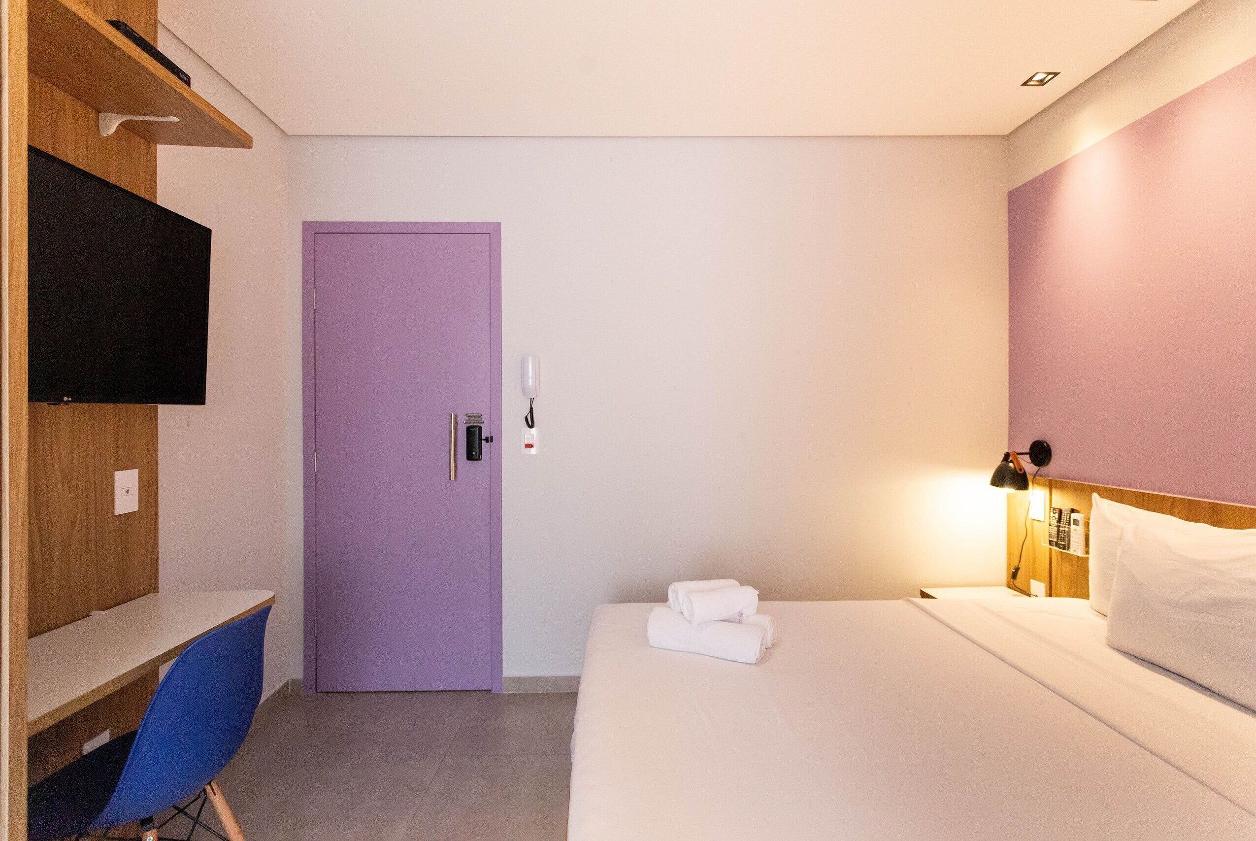 Una habitación de hotel con cama, escritorio, silla, televisor y puerta.