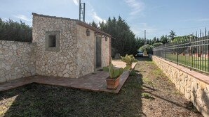 Un bâtiment en pierre doté d’une petite fenêtre et d’une porte, entouré d’une zone pavée agrémentée de plantes en pot.