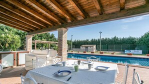 Un espace extérieur avec piscine, comprenant une table dressée pour les repas, entouré d’une pergola en bois et d’une structure en briques.
