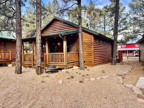 A rustic log cabin with a porch and a fire pit.
