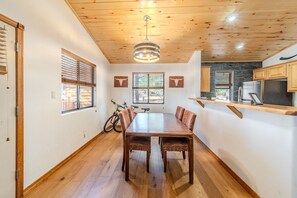 Zona pranzo con tavolo e sedie in legno, ventilatore a soffitto e angolo cottura con frigorifero e fornello.