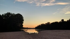 Een strand met kalm water en bomen op de achtergrond.