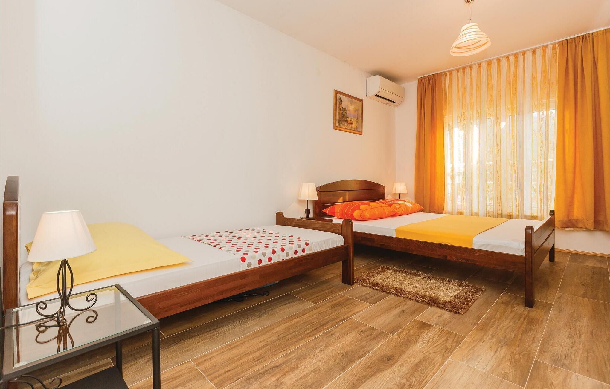Habitación de hotel con dos camas de madera, una mesita con lámpara, un cuadro en la pared y una ventana con cortinas.