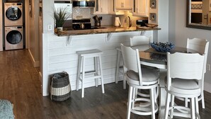 Una cucina moderna con mobili bianchi, un'isola centrale e una zona pranzo con sedie bianche.