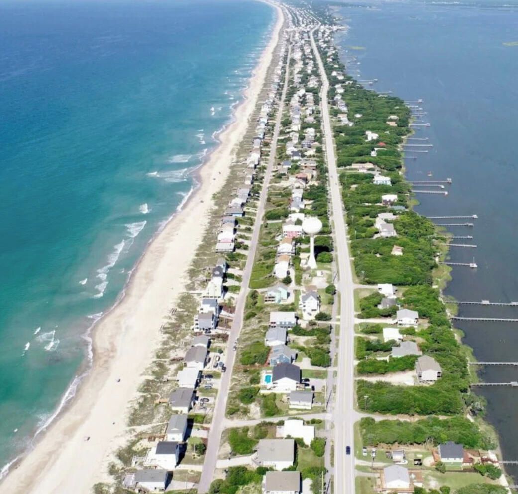 Vista aérea de una zona costera con una extensa playa y una hilera de casas a lo largo de la orilla.