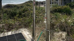 Una casa sulla spiaggia con veranda in legno, doccetta metallica e vista sull'oceano.