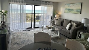 Un soggiorno con balcone vista mare, un divano, un tavolino da caffè e una lampada.