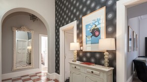 A hallway with a checkered floor, a white arched doorway, a mirror, a cabinet with two lamps, and a framed picture on the wall. - Fantastic corner 2 bedroom property with astounding views of the famous historic Royal Mile. (Edinburgh)