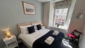 A neatly made bed with white and navy bedding, a bedside lamp, and a framed picture on the wall. - Economical 2 bedroom property just off the famous Royal Mile (Edinburgh)