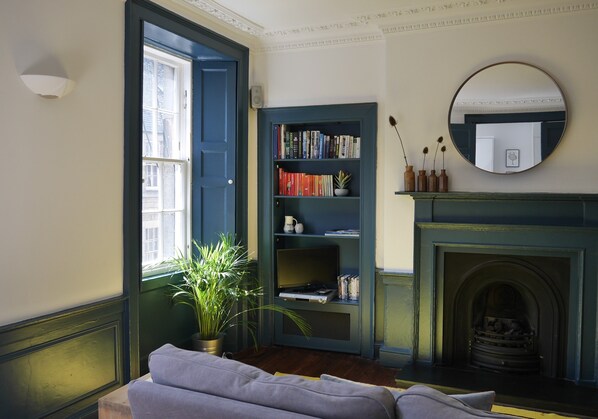 A room with a bookshelf, a fireplace, a mirror, and a window.