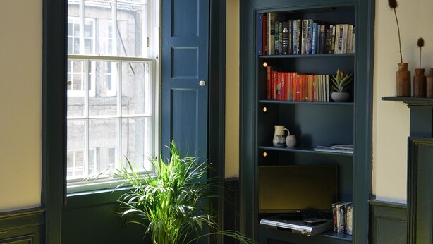 A room with a bookshelf, a potted plant, and a window with a view of buildings. - fantastic 2 bedroom on a bohemian street in Edinburgh's New Town (Edinburgh)