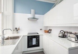 A modern kitchen with white cabinets, a stainless steel sink, a built-in oven, and a kettle on the counter.