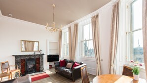 A living room with a fireplace, leather sofas, a dining table, and large windows with curtains. - Incredible 1 bedroom + sofabed on the famous Royal Mile 200 metres from Edinburgh Castle (Edinburgh)