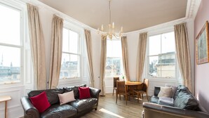 A spacious living room with a brown leather sofa, a smaller sofa, a dining table, and large windows offering a city view. - Incredible 1 bedroom + sofabed on the famous Royal Mile 200 metres from Edinburgh Castle (Edinburgh)