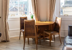 A dining area with a wooden table and chairs, a potted plant, and a view of buildings through large windows.