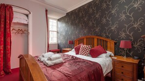 A neatly made bed with a red bedspread, a wooden headboard, and two bedside tables with lamps.