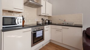A modern kitchen with white cabinets, a stainless steel oven, a microwave, and a black countertop.