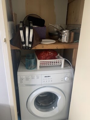 Compact laundry room with a front-loading washing machine and storage for essentials.
