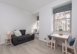 A modern living room with a grey sofa, a small table, and a window with a view of buildings.