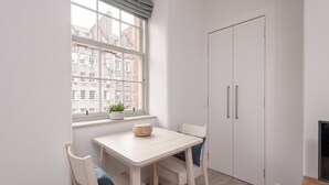 A small, bright room with a white table, two chairs, a window with a view of buildings, and a door.
