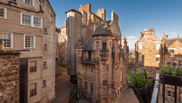 A narrow street with historic stone buildings, including a prominent tower with a dome.