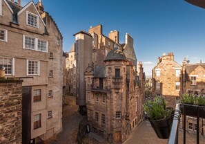 Une rue étroite bordée de bâtiments historiques en pierre, dont une tour imposante surmontée d’un dôme.