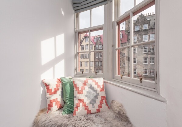 A corner with a window, a fur rug, and two patterned pillows.