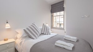 A neatly made bed with striped pillows, a bedside lamp, and folded towels on a white nightstand.
