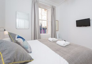 A hotel room with a bed, a TV, a window with curtains, and a view of a building outside. - Wonderful 1 bedroom + sofabed in the heart of the Old Town (Edinburgh)