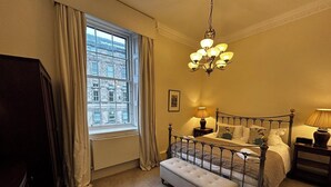 Ein Schlafzimmer mit großem Fenster, einem Bett mit Kopfteil, einer Bank und einer Chandelieber.