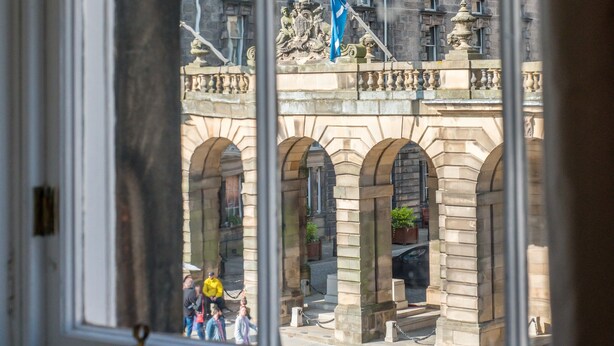 Blick durch ein Fenster eines historischen Gebäudes mit Steinarchitektur, das gewölbte Fenster und eine Flagge zeigt.