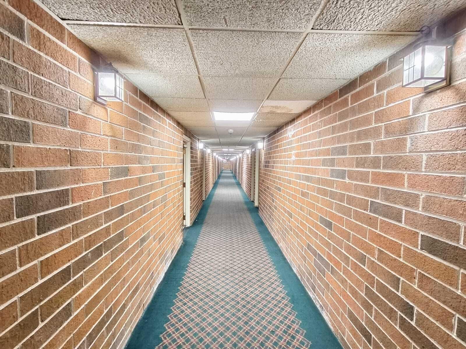 A long, narrow hallway with brick walls and a patterned floor, leading to a series of doors.