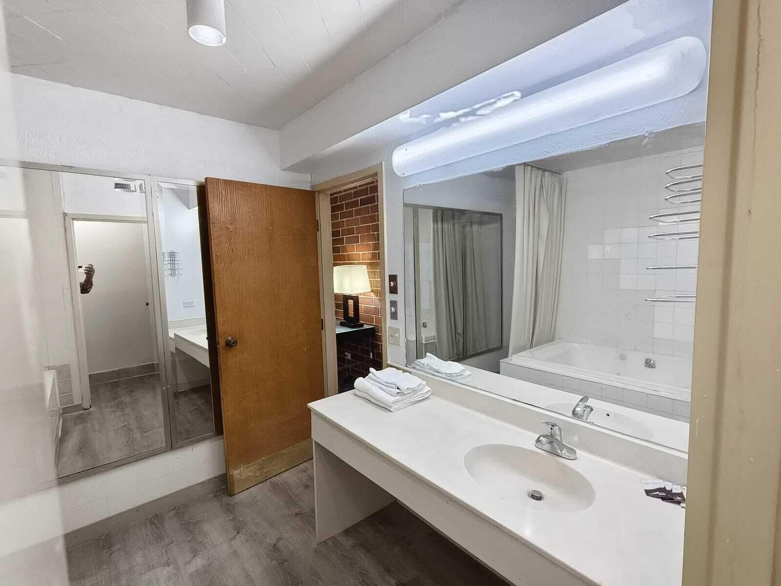 A modern bathroom with a large mirror, white sink, and a wooden door.