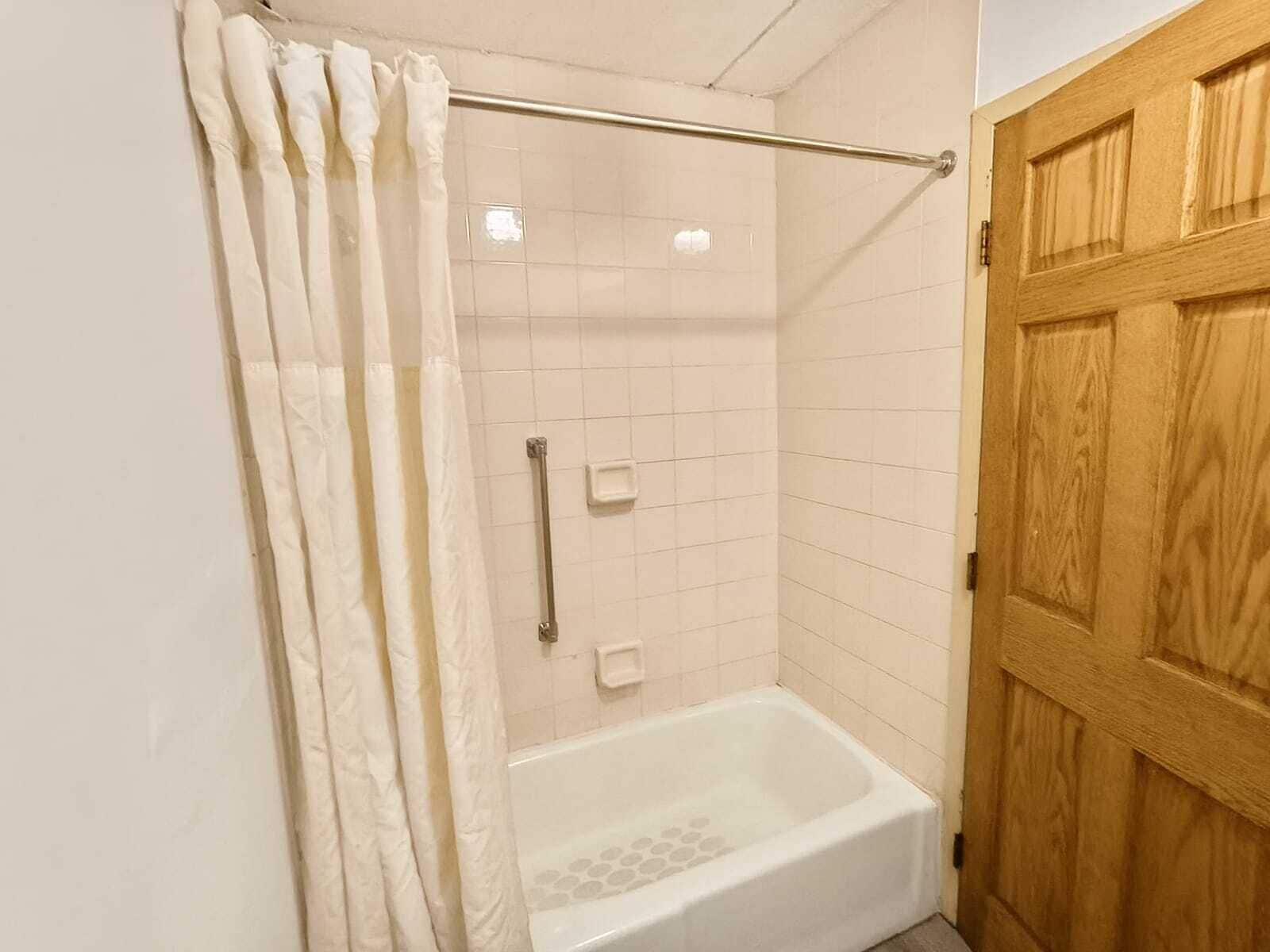 Un baño con ducha, bañera y puerta de madera.