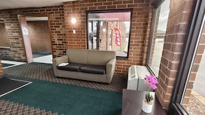A room with a sofa, a small table with a potted plant, a window with a view, and a brick wall.