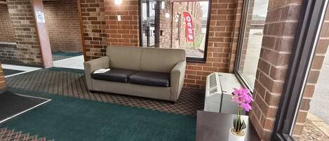 A room with a sofa, a small table with a potted plant, a window with a view, and a brick wall.
