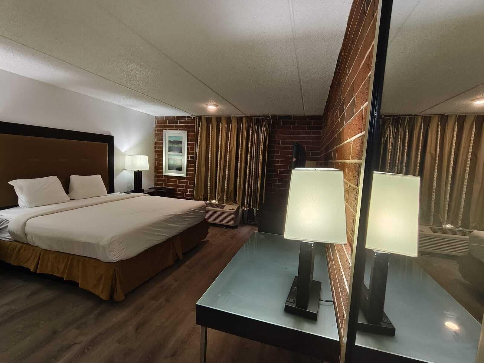 A hotel room with a bed, bedside lamps, a mirror, and a window with curtains.