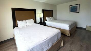 Una camera d'albergo con due letti singoli, un comodino con una lampada, un quadro incorniciato appeso al muro e un pavimento in legno.
