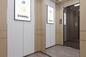 A hallway with framed Chanel logos on the walls, a glass elevator door, and a control panel. - Yulin Hotel (Yuchai Shop) (Yulin)