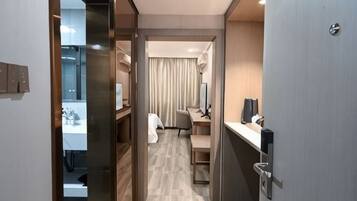 A narrow hallway leading to a bedroom with a desk, chair, and a bed.