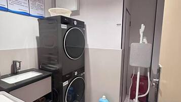 Une chambre d’hôtel de taille réduite, équipée d’une machine à laver, d’un petit lavabo et d’un miroir.