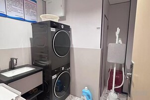 Habitación de hotel pequeña con lavadora, un lavamanos y un espejo.