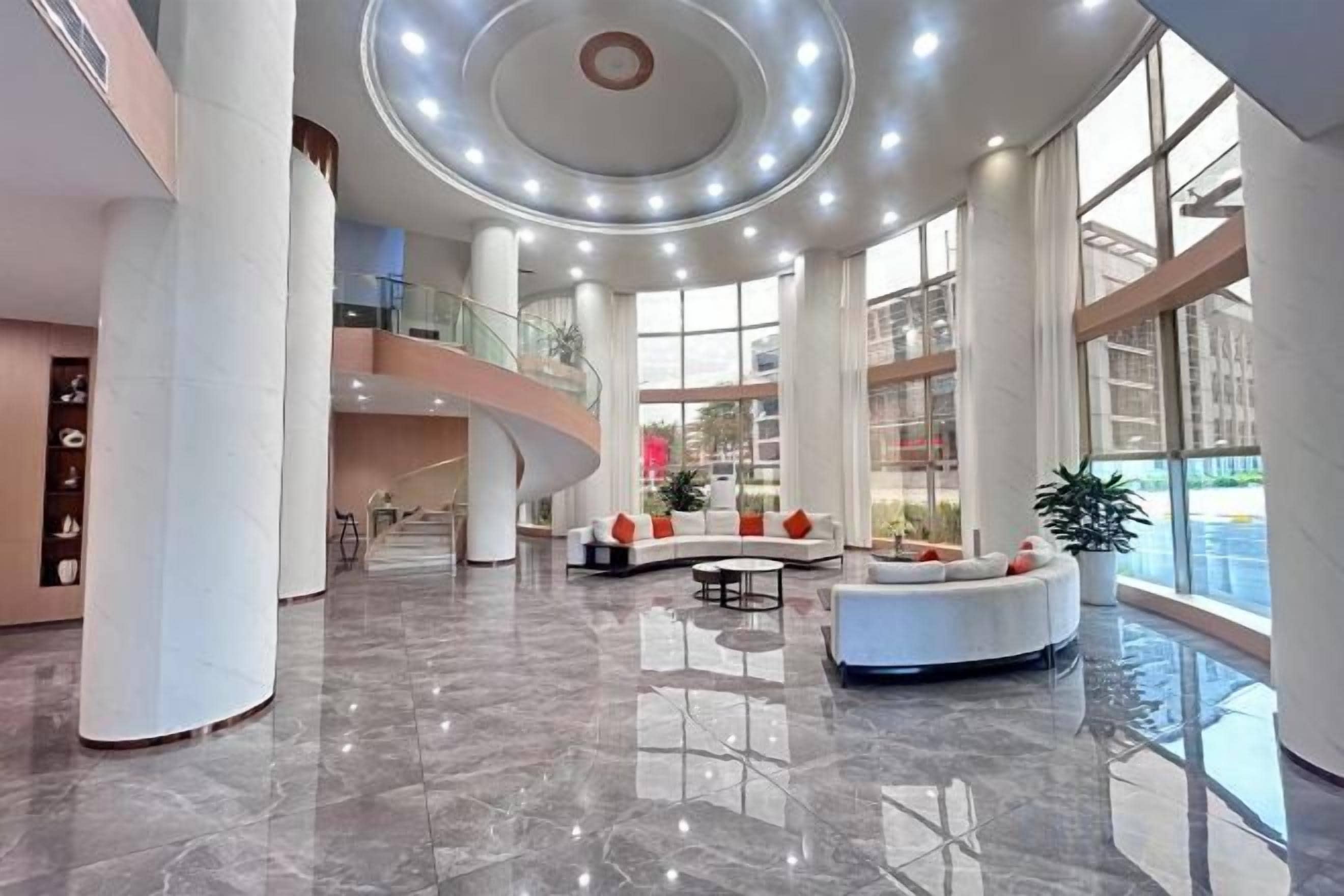 A spacious lobby with a curved reception desk, large windows, and a high ceiling with circular lighting.