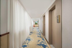 Pasillo de hotel con piso alfombrado, puertas a la derecha y una recepción a lo lejos.