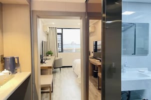 Habitación de hotel con cama, escritorio, televisor y baño con lavamanos y espejo.